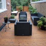 Outdoor rooftop patio with black wicker furniture on a wooden deck, surrounded by potted plants and brick walls.